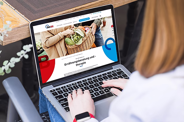 Eine Person tippt auf einer Laptop-Tastatur, während eine Webseite zur Ernährungsberatung angezeigt wird.