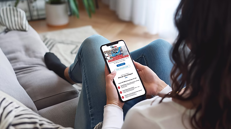 Eine Person sitzt gemütlich auf einem Sofa und nutzt ein Smartphone, um eine App mit Dienstleistungen zu entdecken.