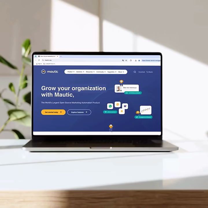Ein Laptop auf einem weißen Tisch zeigt die Mautic-Website mit der Überschrift 'Grow your organization with Mautic'. Die Animation hebt verschiedene Funktionen der Open-Source-Marketing-Automation-Plattform hervor.