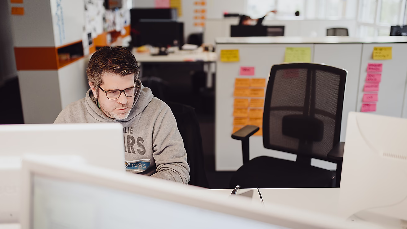Ein Mann arbeitet konzentriert am Computer in einem modernen Büroraum.