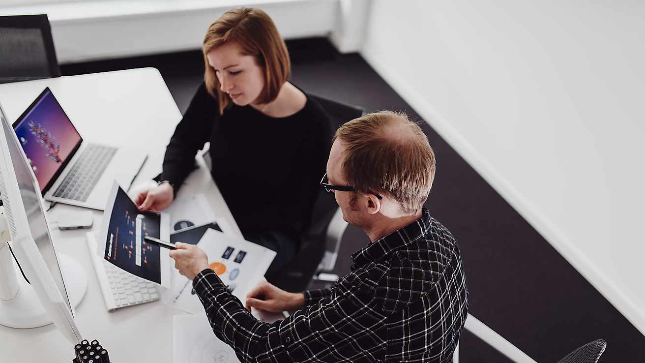 Ein Mann und eine Frau sitzen an einem Tisch und besprechen Grafiken zur Customer Journey auf einem Ausdruck vor ihnen.