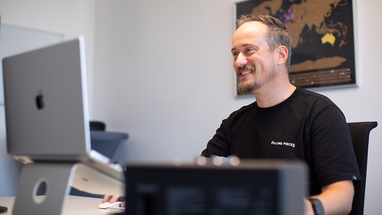 Ein Mann sitzt lächelnd an einem Schreibtisch vor einem Computer und arbeitet konzentriert.