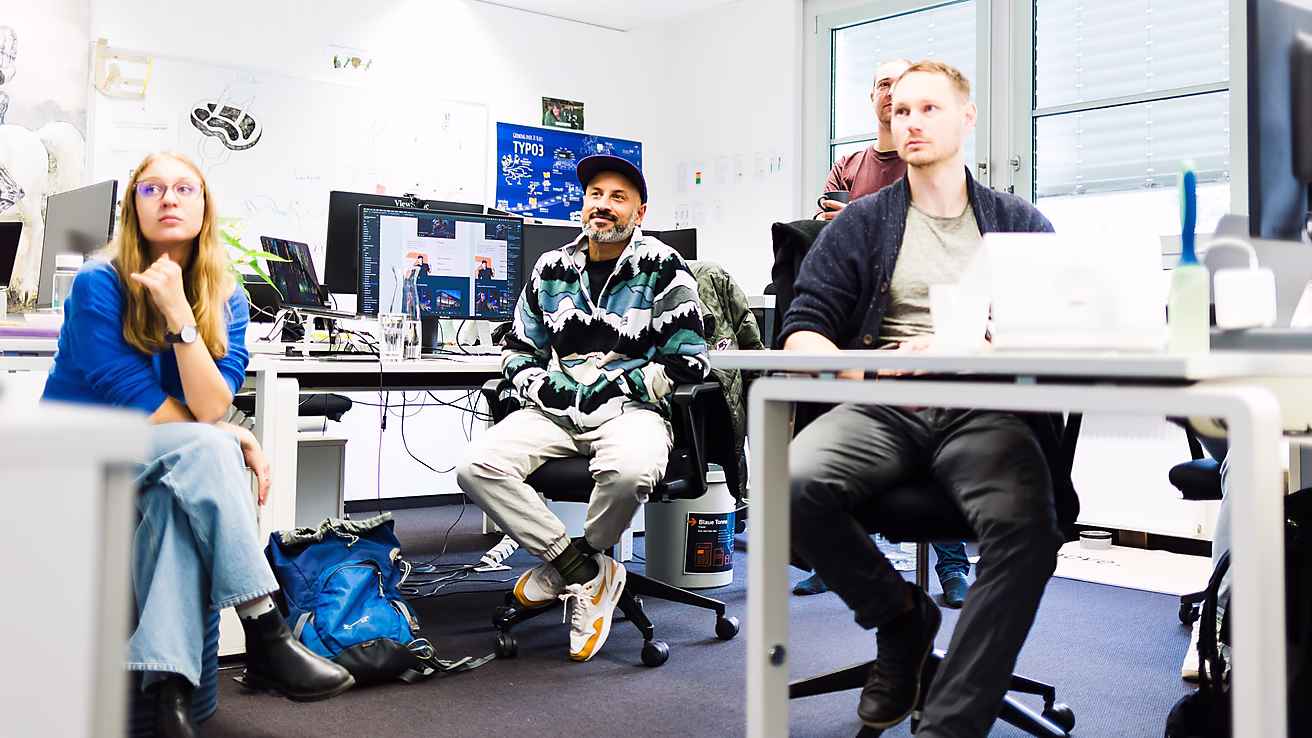 Eine Gruppe von Menschen schaut aufmerksam auf Computerbildschirme in einem modernen Büro. Sie diskutieren oder lernen zusammen.