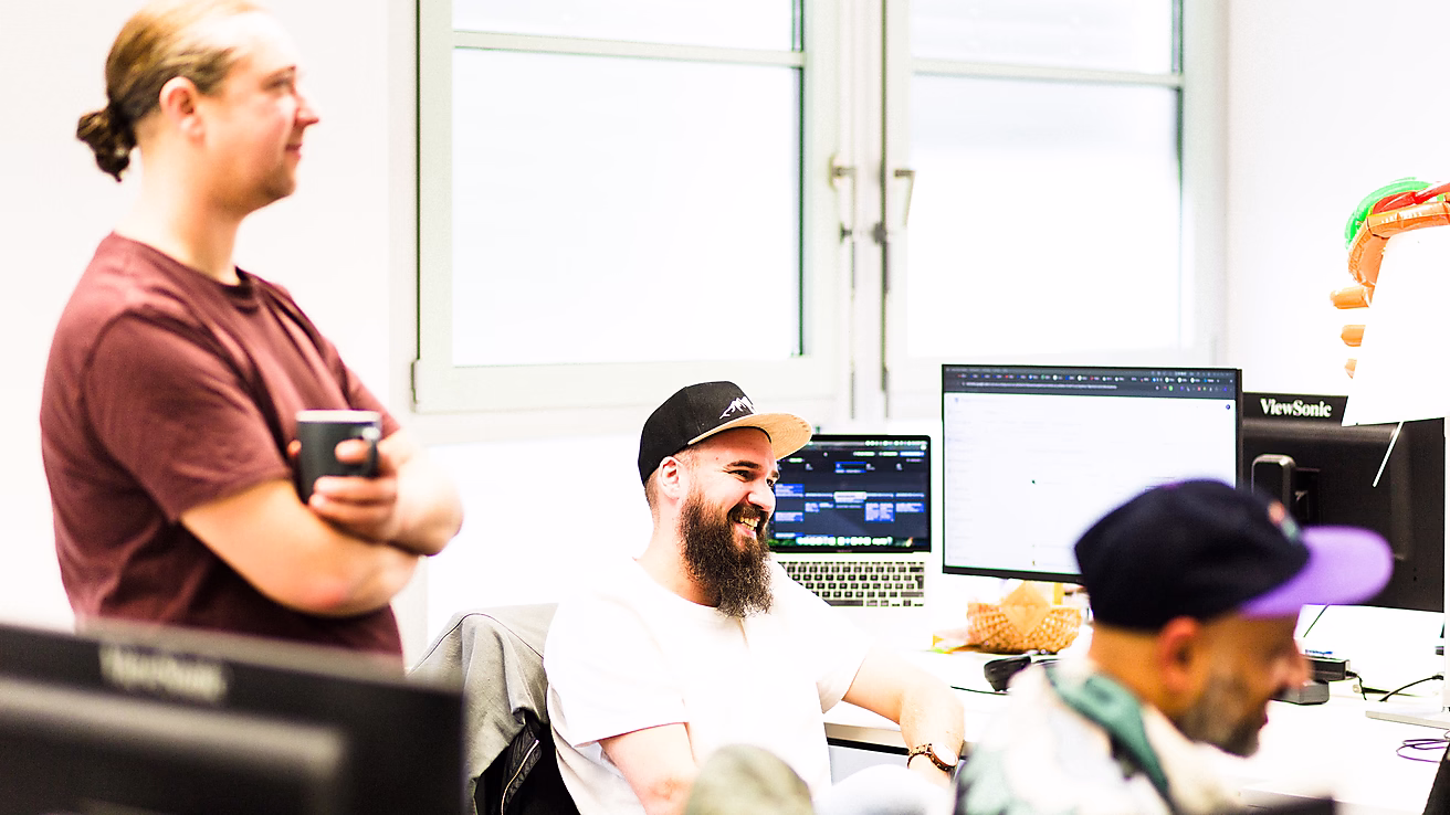Drei Mitarbeiter lachen zusammen in einem Büro während eines Meetings zur SEO-Strategie.