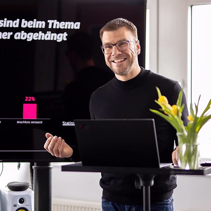Ein lächelnder Mann präsentiert Daten zu Künstlicher Intelligenz, mit einem Diagramm, das 64% und 22% zeigt. Blumen sind im Vordergrund.