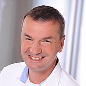 Ein lächelnder Mann mit kurzen Haaren trägt ein weißes Hemd und blickt freundlich in die Kamera.