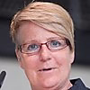 Porträt einer Person mit blonden, kurzgeschnittenen Haaren und Brille, die in die Kamera lächelt.