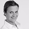 Eine Person lächelt in die Kamera, trägt ein weißes Hemd und hat kurze Haare. Der Hintergrund ist hell und neutral gehalten.